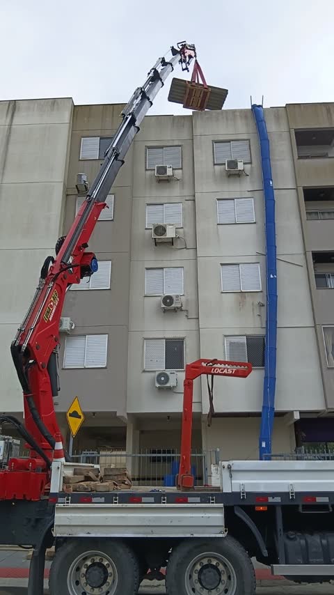 Guindaste articulado levando material até o alto de um prédio residencial