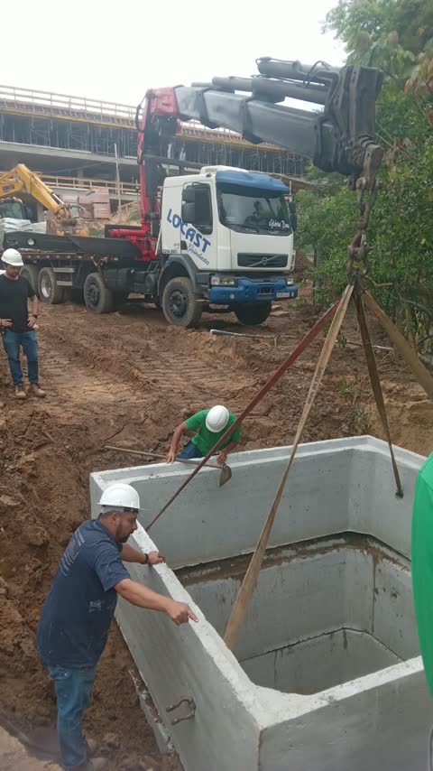 Içamento de caixa de concreto pré-moldada para dentro de uma vala, com a equipe em campo