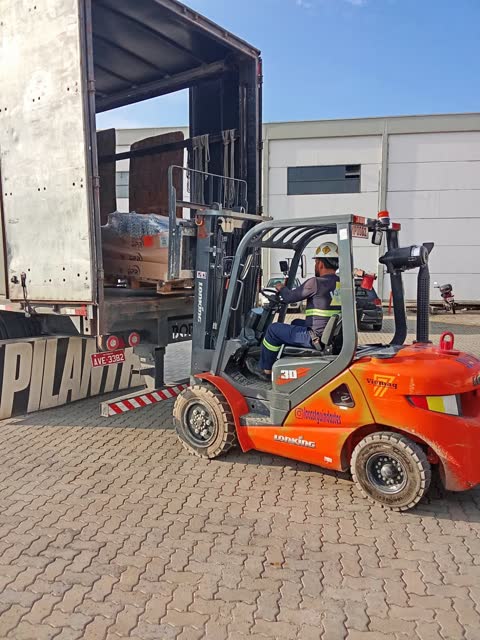 Empilhadeira descarregando carreta em pátio industrial