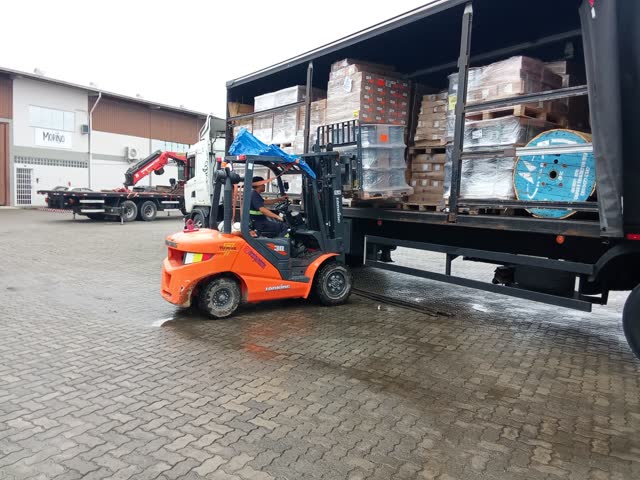 Empilhadeira descarregando carga de caminhão em pátio