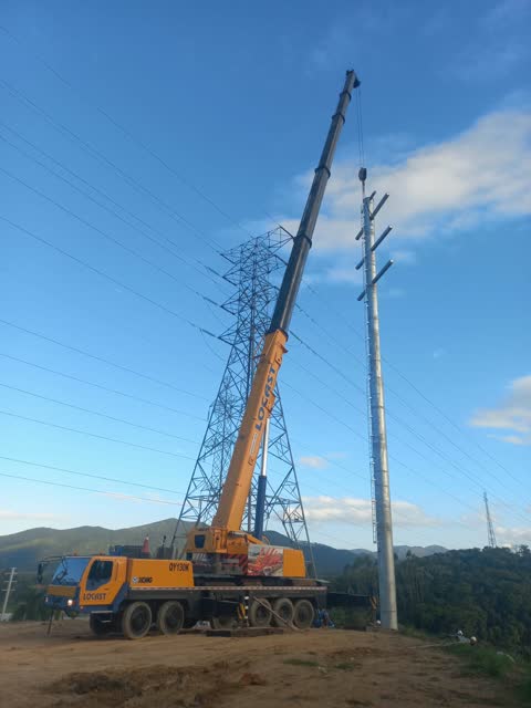 Guindaste telescópico ao lado de torre de transmissão e poste de energia